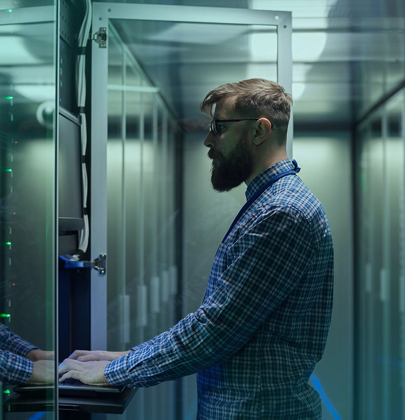 Administrator IT pracuje przy szafie serwerowej w centrum danych, obsługując sprzęt i monitorując infrastrukturę.